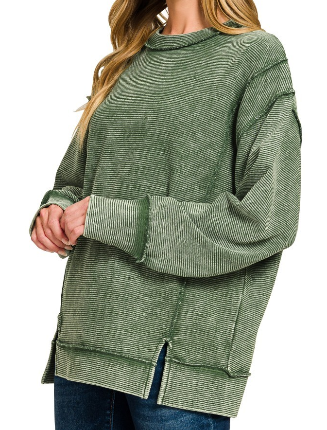 Model wearing acid washed ribbed exposed seam pullover in dark green with long sleeves and side slits.