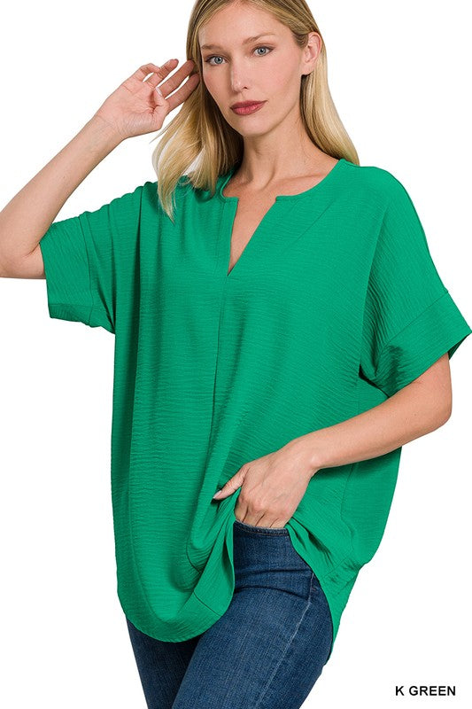 Woman wearing a Kelly green airflow V-neck top with cuffed sleeves and a relaxed fit, available in sizes S-3X.
