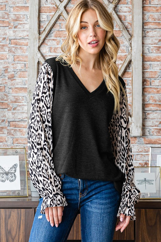 Model wearing a black knit top with leopard print balloon sleeves and blue jeans.