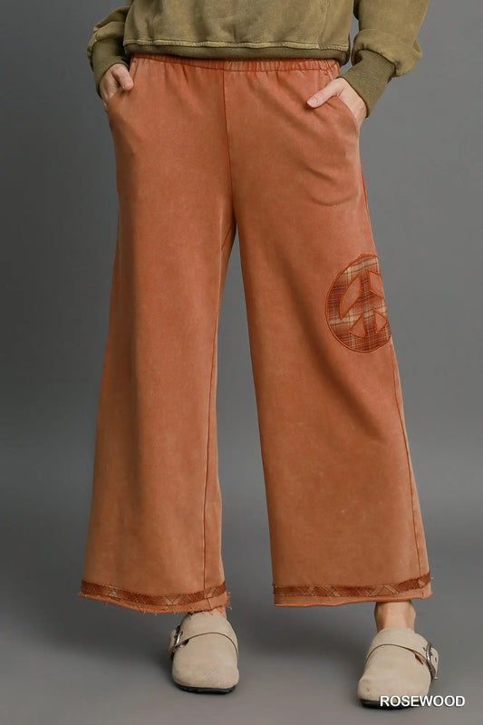 Rosewood wide-leg pants with plaid peace-sign patch and raw hem detail, styled with beige clogs