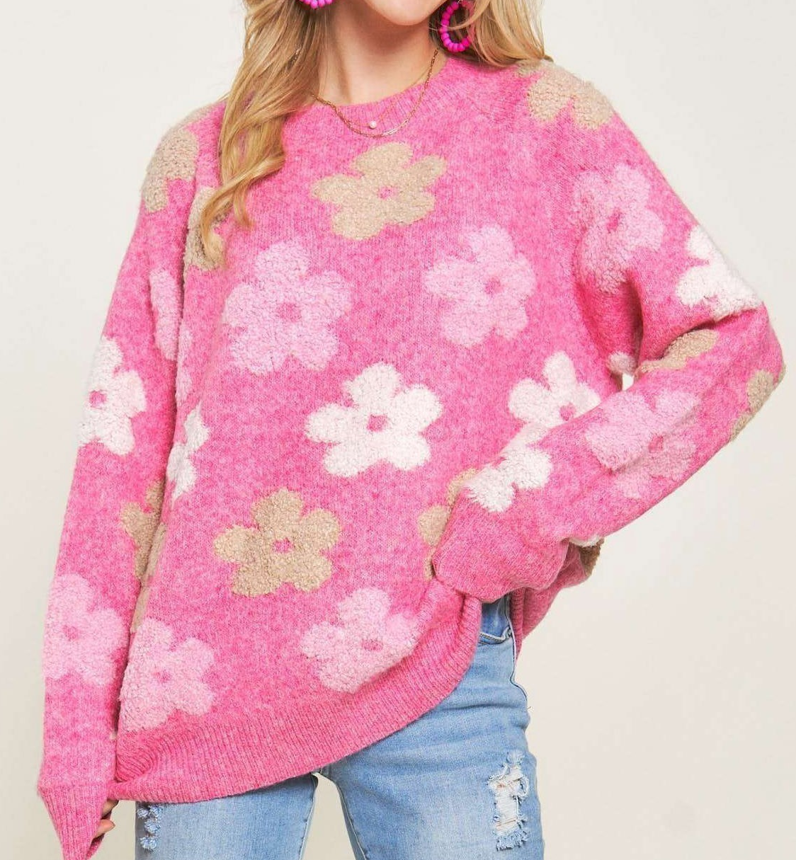 Pink fuzzy knit sweater with allover floral pattern, long sleeves, and relaxed fit, styled with light wash distressed jeans.