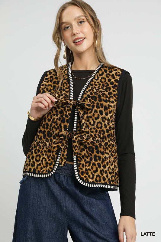 Woman wearing a sleeveless leopard print vest with bow tie front and contrast striped trim over a black long sleeve top.