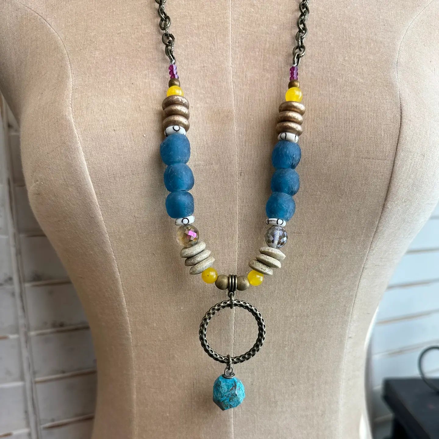 Boho necklace with blue glass beads, yellow accents, and bronze ring with turquoise drop on dress form