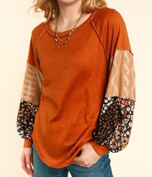 Woman wearing a burnt orange knit top with mixed print balloon sleeves featuring floral and lace patterns.