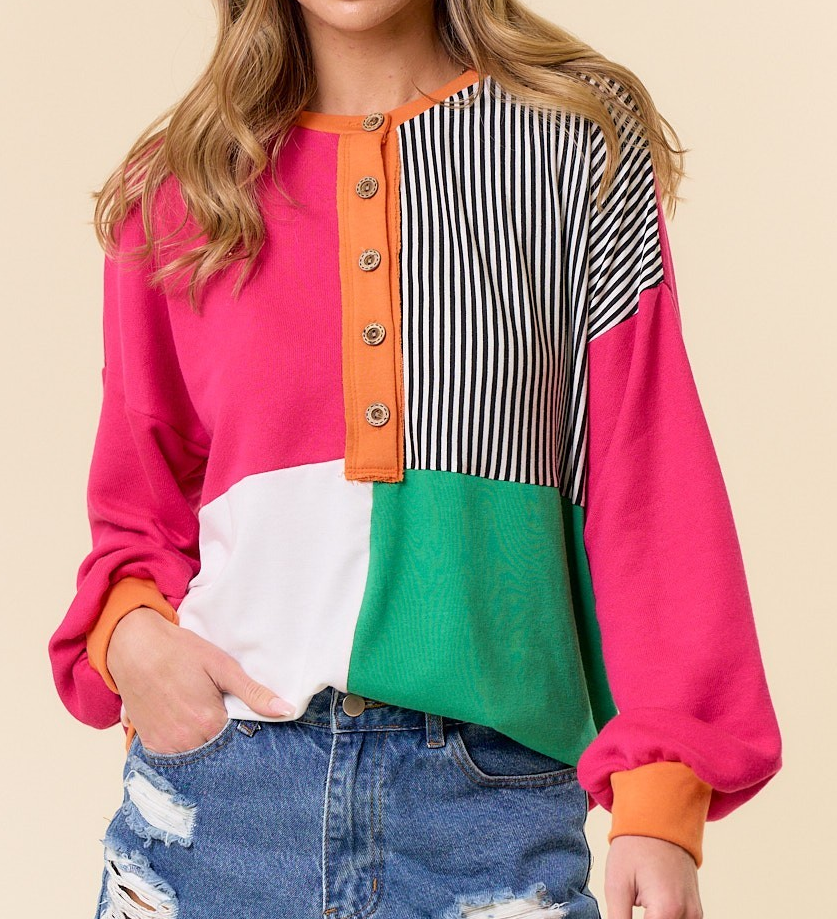 Colorblock relaxed fit pullover with pink, green, white, and striped panels, featuring a button neckline and long sleeves styled with distressed denim.