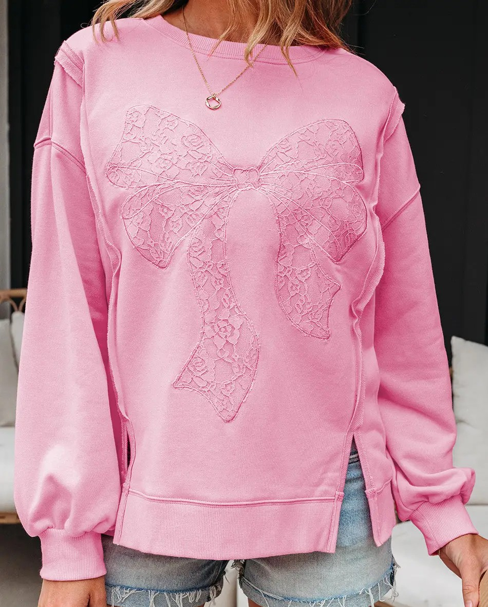 Pink long sleeve pullover featuring a lace bow patchwork detail on the front, styled with denim shorts for a casual feminine look.
