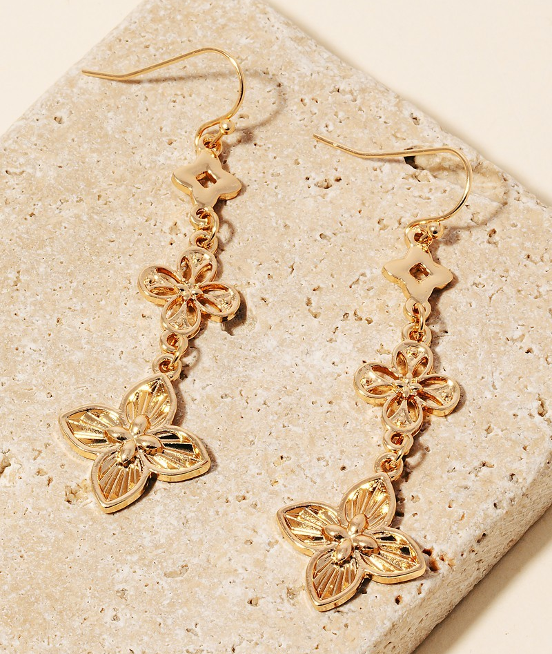 Gold-tone triple clover drop earrings with intricate floral designs, approximately 2 inches long, shown on textured stone background.