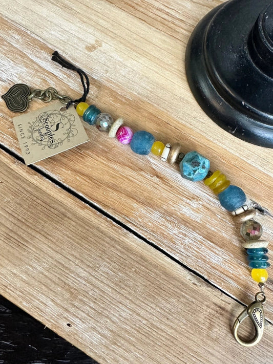 Boho beaded bracelet with blue, yellow, and pink accents and antique bronze clasp on wood background

