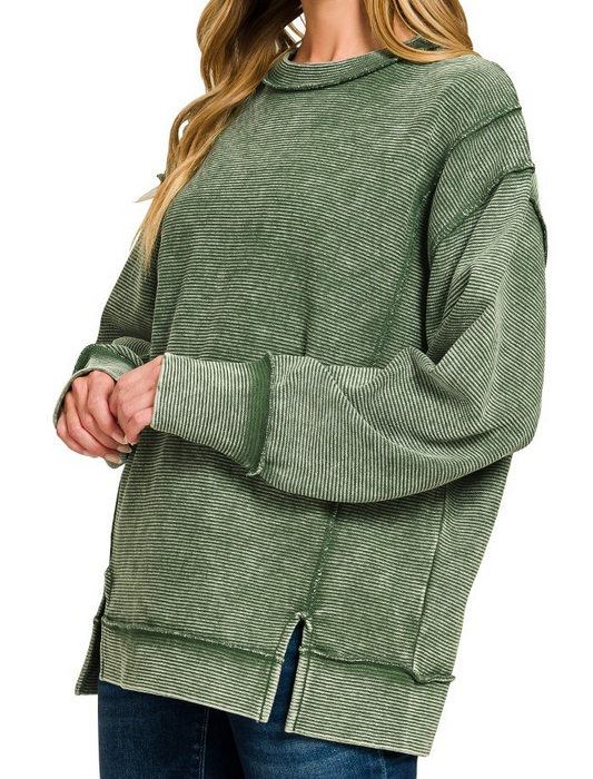 Model wearing acid washed ribbed exposed seam pullover in dark green with long sleeves and side slits.