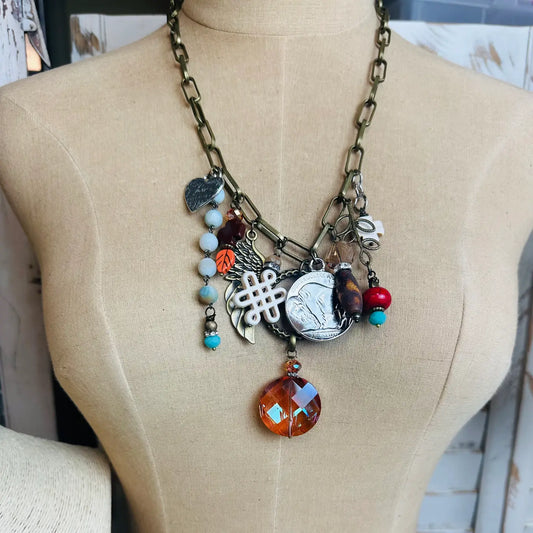 Chunky bronze charm necklace with assorted vintage pendants and amber crystal drop on dress form

