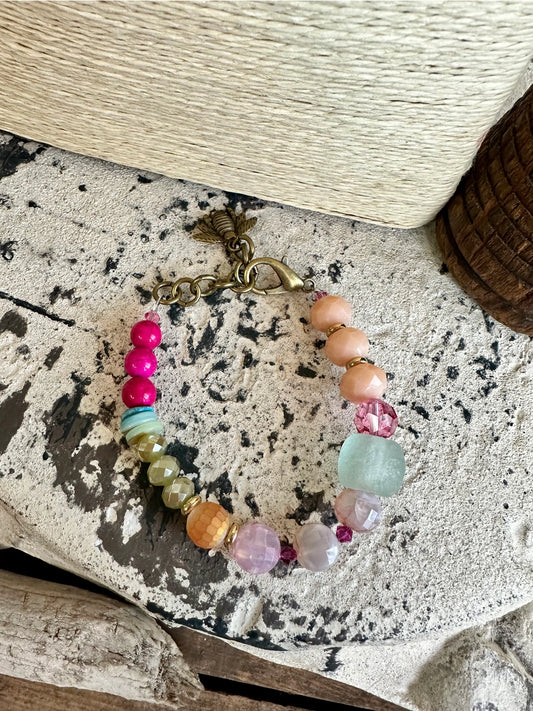 Colorful beaded bracelet with seaglass, crystal, and bronze clasp on neutral textured surface

