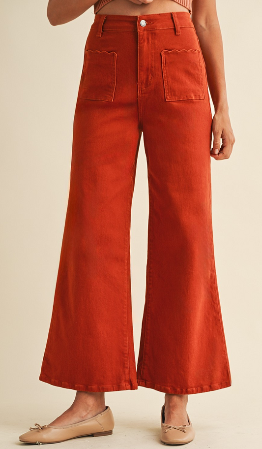 Rust wide-leg high-rise pants with scalloped front pockets, shown with neutral flats.