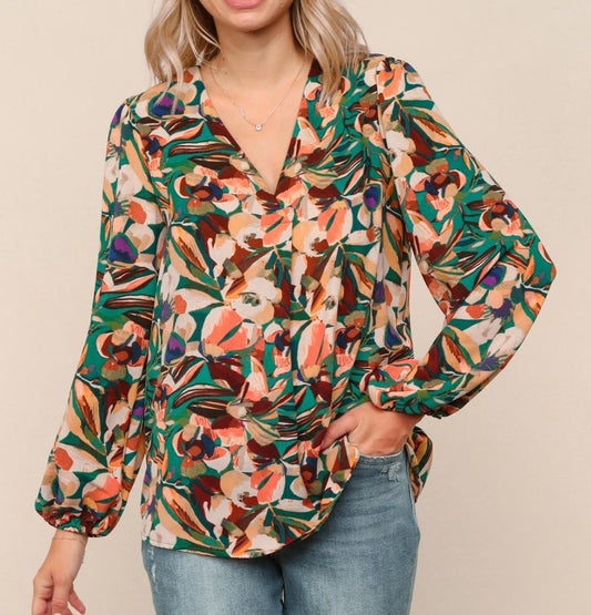 Woman wearing a vibrant floral print blouse with long sleeves and V-neckline, styled with denim jeans.