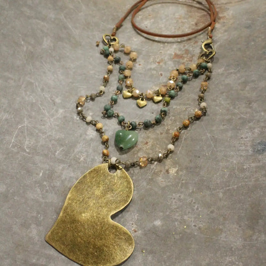 Layered boho necklace with green heart charm, small brass hearts, and a large hammered brass heart pendant on a leather cord.