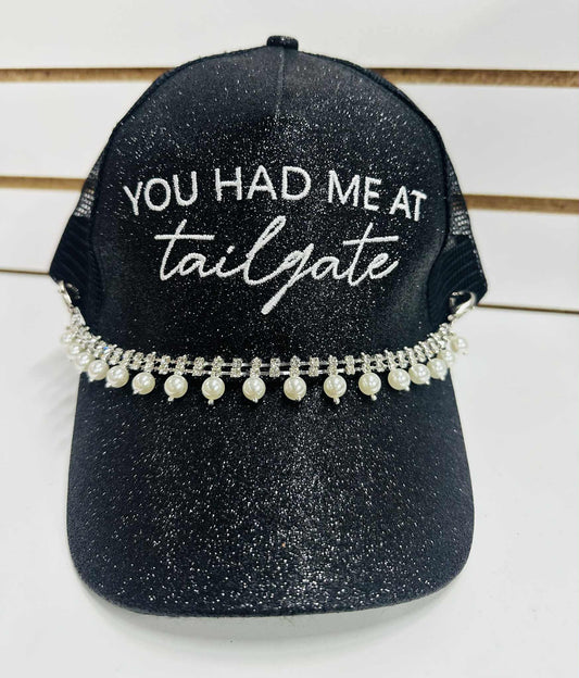 Black glitter trucker hat with “You Had Me at Tailgate” embroidery, pearl rhinestone trim, and mesh back with pearl accents.