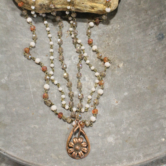 Triple-strand necklace with copper daisy pendant, featuring ivory and amber glass beads.

