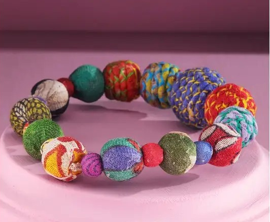 Colorful fabric beaded stretch bracelet with multicolor textured beads on a pink background