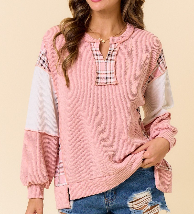 Pink ribbed pullover with plaid accent neckline, shoulders, and side panels, featuring long sleeves and a relaxed fit styled with distressed denim.