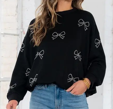 Black crew neck long sleeve top featuring all-over crystal bow embellishments, worn with light denim jeans.