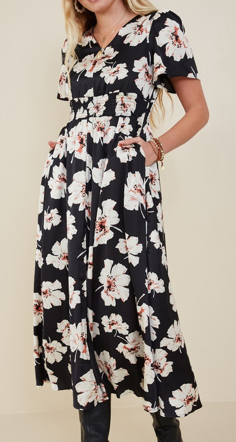 Model wearing a black midi dress with white and blush floral print, smocked waist, and short flutter sleeves.
