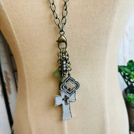 Antique bronze necklace with cross, key, rhinestone charm, and decorative pendant on dress form

