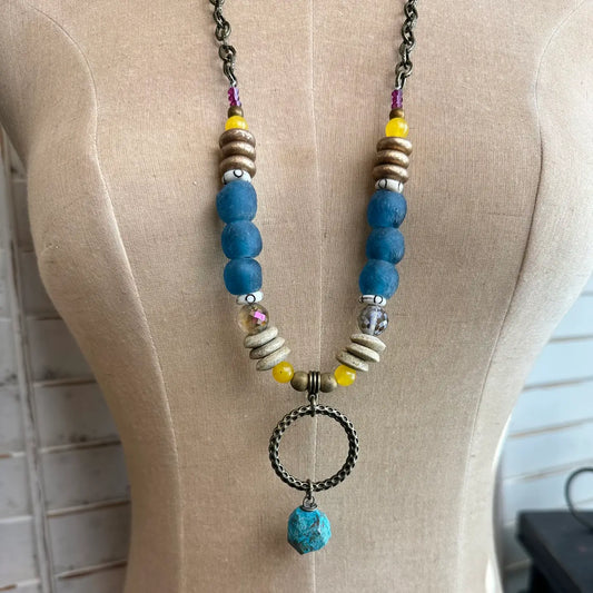 Boho necklace with blue glass beads, yellow accents, and bronze ring with turquoise drop on dress form

