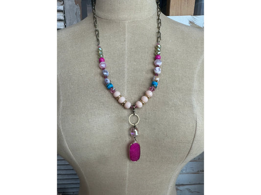 Colorful beaded necklace with pink gemstone pendant on mannequin display

