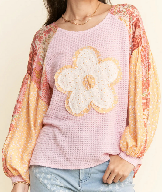 Pink waffle knit top with patchwork floral sleeves and large white daisy applique.

