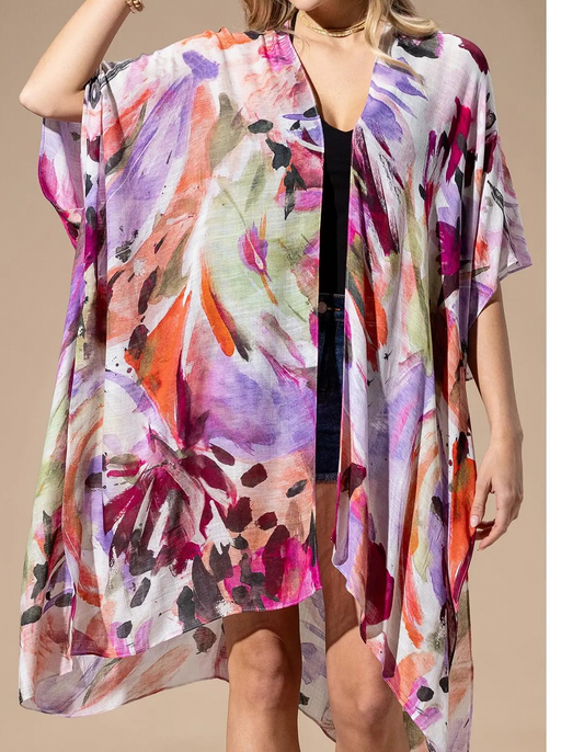 Woman wearing a colorful lightweight kimono with a watercolor floral pattern over a black tank and shorts.