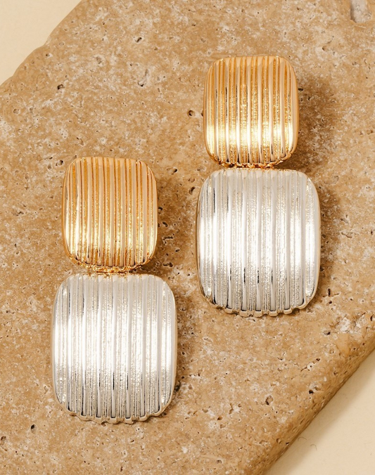 Gold and silver ridged rectangular drop earrings on stone background.