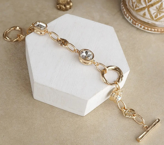Gold link bracelet with clear crystal accents and toggle clasp displayed on a neutral background.
