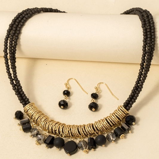 Black and gold statement necklace set with matching beaded earrings on a neutral background.