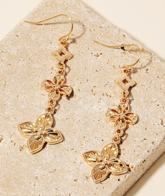 Gold-tone triple clover drop earrings with intricate floral designs, approximately 2 inches long, shown on textured stone background.